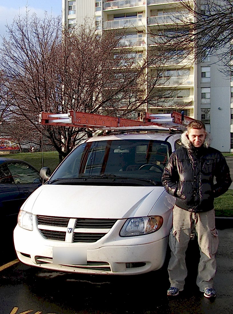 Denis Valasevich in 2009 beside his first work van, two extension ladders strapped to the roof rack, outside a Toronto apartment tower