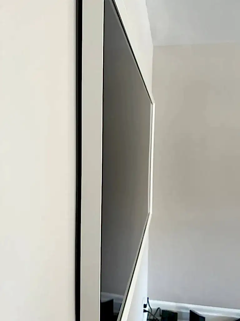 Edge-on view of a flush-mounted TV with a white frame, showing almost no gap between the panel and the wall