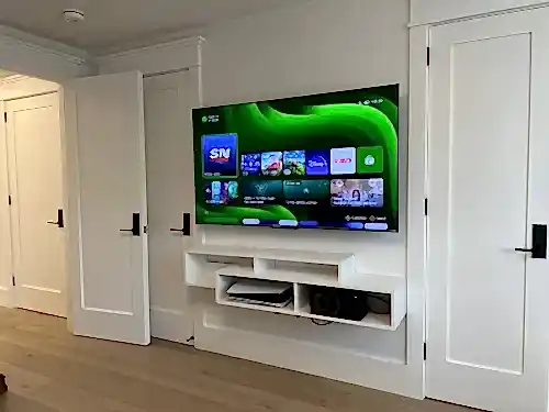 TV mounted on white built-in millwork between two doors, above floating shelves holding a console and centre speaker