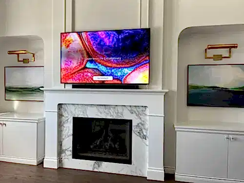 TV mounted above a white painted mantel and marble fireplace surround, between two arched niches with picture lights