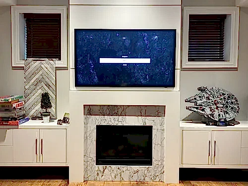 TV mounted above a marble fireplace surround, framed by white built-in cabinetry and upper cupboards