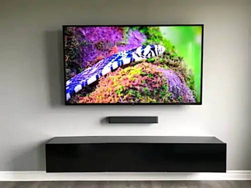TV with a compact soundbar mounted below on a grey wall, above a long black floating console