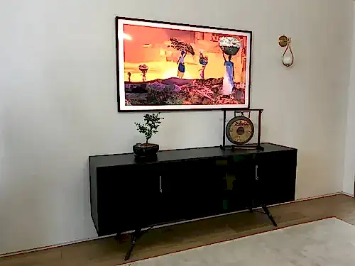 Samsung Frame TV in a black bezel showing artwork in Art Mode above a black sideboard