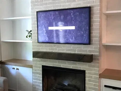 TV mounted on a painted white brick chimney breast above a rustic timber mantel, between white shelving