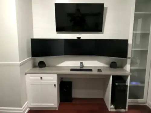 Home office with a wall-mounted TV above a three-monitor desk setup and tower PC