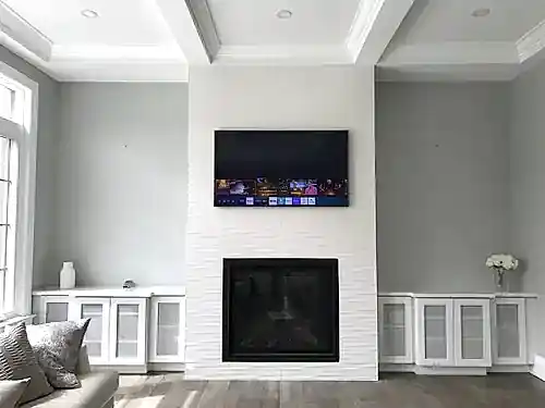 TV mounted on a white textured chimney breast above a modern gas fireplace, flanked by glass-front cabinets