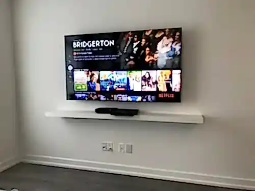 TV mounted on a white wall above a long floating shelf holding a soundbar and a streaming box
