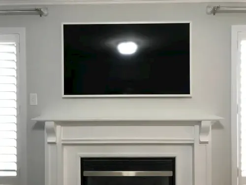 Samsung Frame TV in a white bezel, screen off, mounted above a traditional painted mantel
