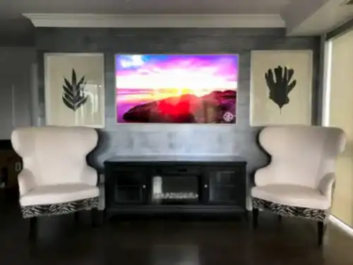 TV mounted on a grey wood panelled wall between two framed prints, above a media cabinet with a fireplace insert