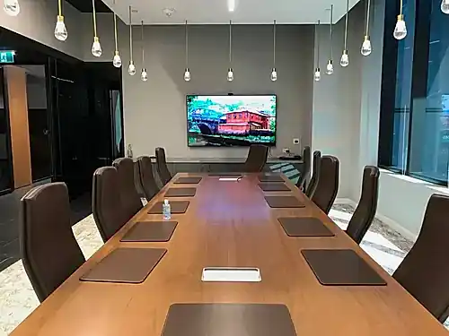 TV mounted at the head of a boardroom table under a run of pendant bulbs