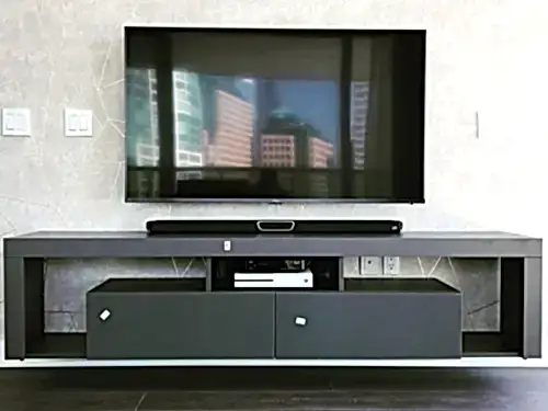 TV and soundbar mounted on a textured patterned wall above a grey console holding AV gear and a games console