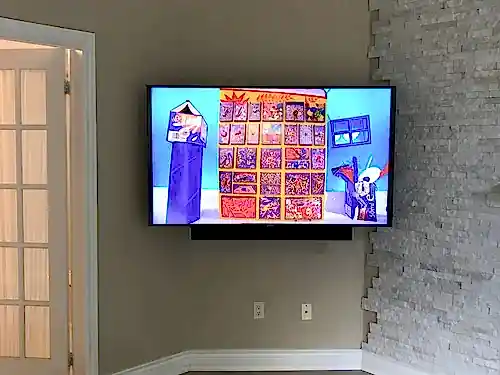 TV and soundbar mounted beside a stacked stone corner in a beige living room