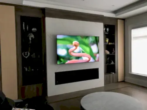 Wider view of a TV on a marble panel with glass display cabinets either side and a linear fireplace below