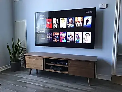 Large TV mounted flush on a pale blue-grey wall above a walnut console