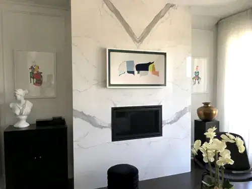 Samsung Frame TV showing abstract artwork, mounted on a marble slab above a recessed fireplace