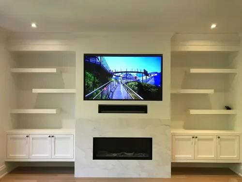 TV and soundbar mounted above a marble fireplace surround, between floating shelves and built-in cabinets