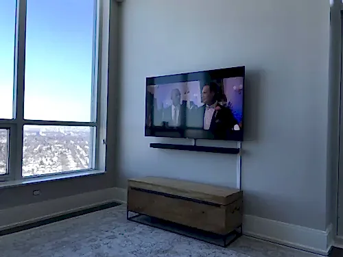 TV and soundbar mounted on a condo wall beside floor-to-ceiling glass, cables run in a slim vertical channel