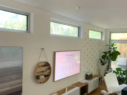 Samsung Frame TV in a white bezel on a bright studio wall below a row of clerestory windows