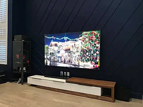 TV and soundbar mounted on a navy diagonal slat feature wall above a white and walnut console