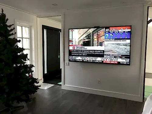 TV mounted on a white foyer wall showing a news channel, beside the front entry