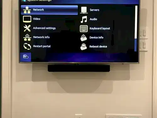 TV and soundbar mounted on a beige wall above paired outlet and low-voltage plates for the concealed cable run