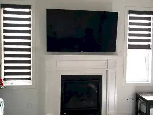 TV mounted above a traditional painted mantel and gas fireplace, between two blinded windows