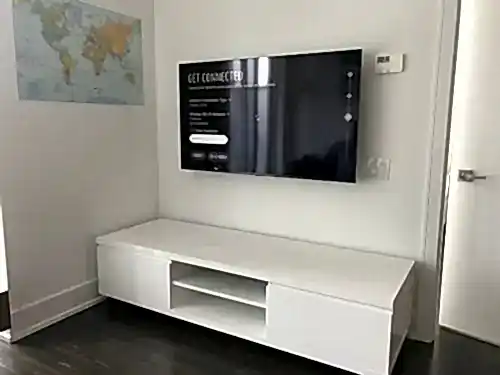 TV mounted on a white wall beside a framed world map, above a low white console