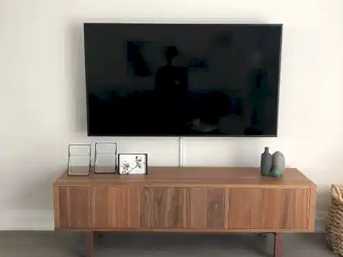 TV on a tilting mount above a walnut sideboard, with a single cable dropped to the equipment below