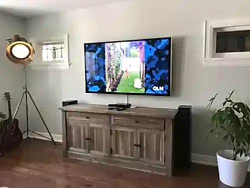 TV mounted on a pale green wall above a weathered wood sideboard, with a floor speaker alongside