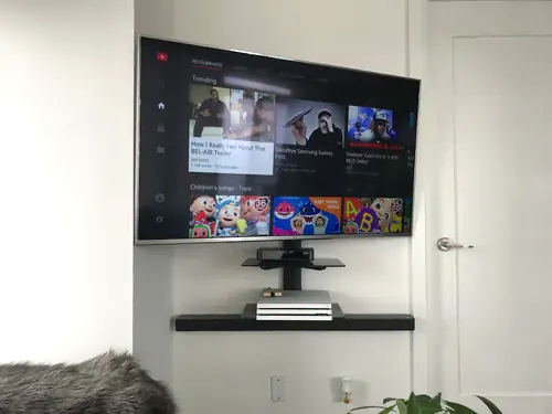 TV, soundbar and a glass AV shelf mounted together on a white wall