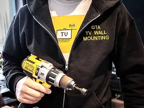 GTA TV Wall Mounting installer in branded workwear holding a cordless impact driver