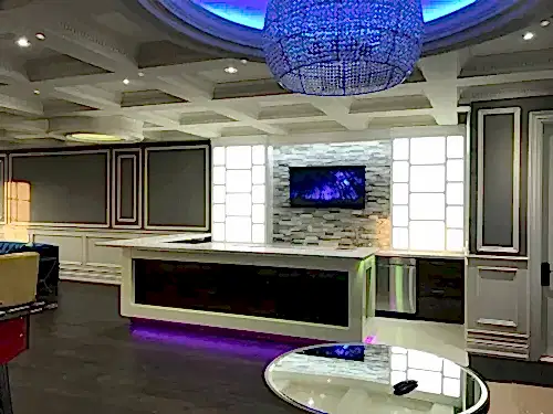 TV mounted on a stone mosaic backsplash in a large entertaining bar under a crystal chandelier