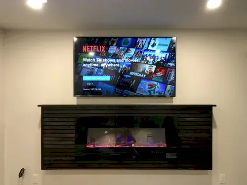 TV mounted above a dark slatted wall unit housing a linear electric fireplace in a basement