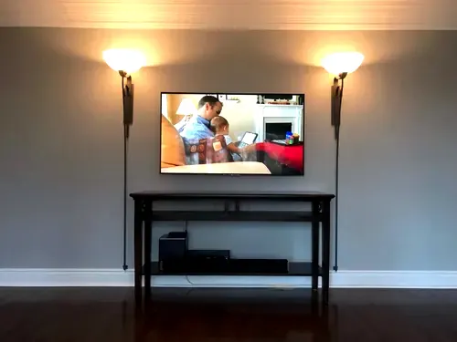 TV mounted on a grey wall between two wall-mounted swing arm lamps, above a black console table