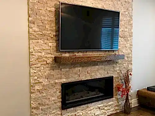 TV mounted on a travertine ledgestone chimney above a timber mantel and linear fireplace