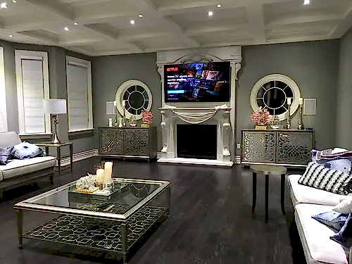 TV mounted above a carved white marble mantel in a formal living room with mirrored consoles