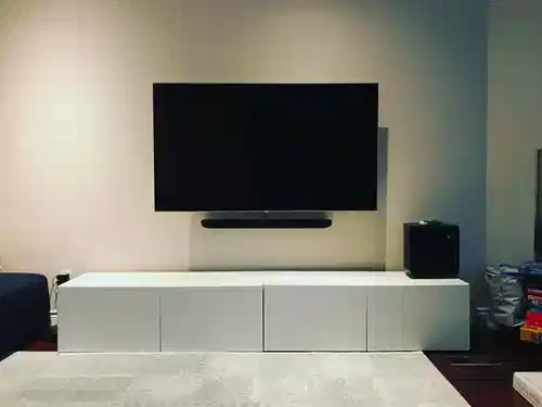 TV and soundbar mounted on a cream wall above a white console, with a subwoofer alongside