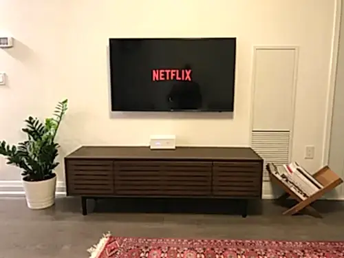 TV mounted flush on a cream wall above a slatted walnut console