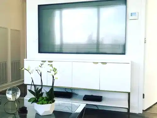 Large TV mounted on a white panel wall above a white and brass sideboard