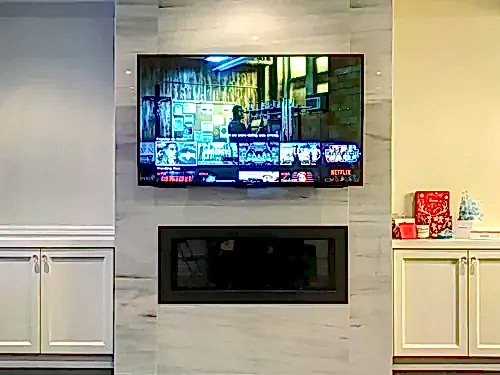 TV mounted on a marble-look porcelain chimney above a linear fireplace, between white cabinets