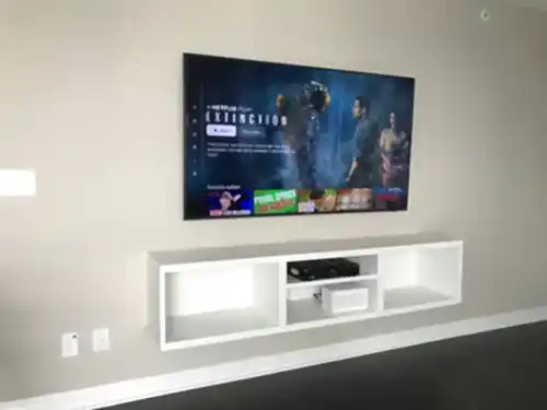 TV mounted on a beige wall above a white floating media cubby, with the outlet and cable plates alongside