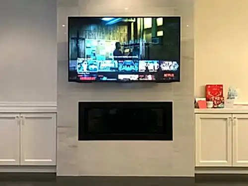 TV mounted on a porcelain slab chimney above a linear fireplace, flanked by white cabinetry