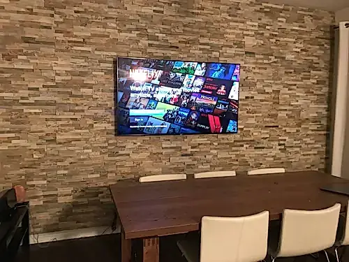 TV mounted on a reclaimed timber plank feature wall above a dining table