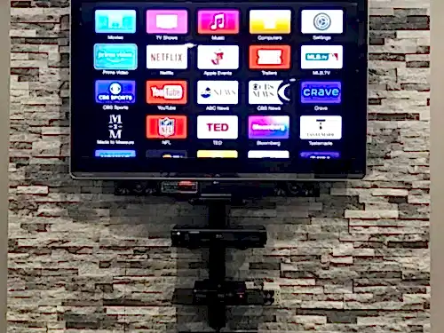TV mounted on a stacked stone wall with the AV equipment carried on a bracket shelf and the cabling gathered below
