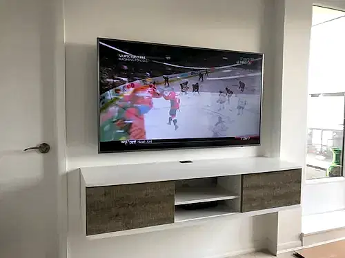 TV mounted on a white wall above a floating console with grey wood drawers