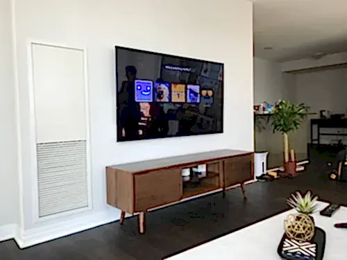 TV mounted on a white wall above a walnut mid-century console in a bright condo