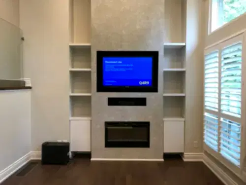 TV recessed into a plaster chimney breast above a linear fireplace and a centre speaker slot, between white bookcases