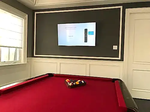 TV mounted on a dark grey panelled accent wall above wainscoting in a games room