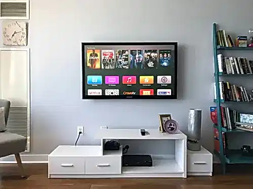 TV mounted on a pale wall above a white console, beside a blue ladder bookshelf