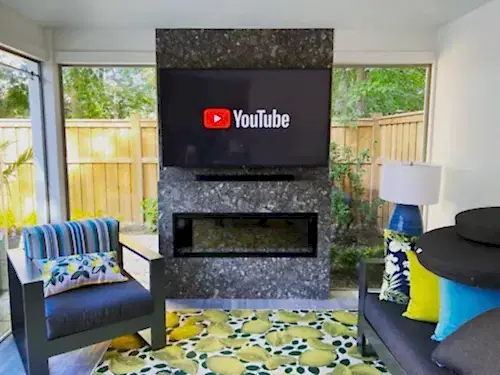 Flat screen mounted on a dark granite fireplace surround above a linear insert in a covered patio room